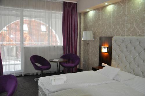 a hotel room with a bed and two purple chairs at Bástya Konferencia és Wellness Hotel in Miskolctapolca