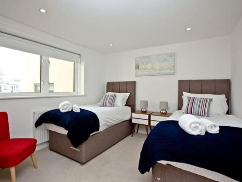 a bedroom with two beds and a red chair at 15 Ocean Gate Newquay in Crantock