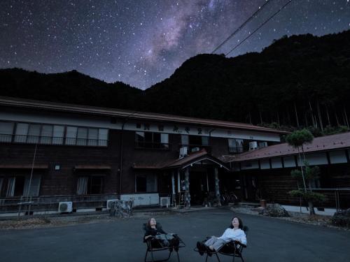 two women sitting on chairs in front of a building at night at 民宿みやま in Ōno