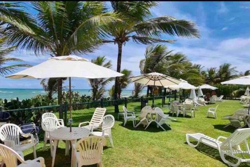 a group of chairs and tables with umbrellas and the ocean at Seu cantinho no paraíso de Guarajuba - Bahia in Guarajuba