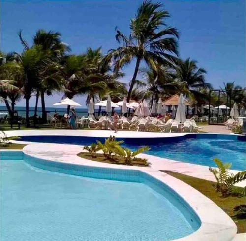 una piscina in un resort con palme e oceano di Seu cantinho no paraíso de Guarajuba - Bahia a Guarajuba