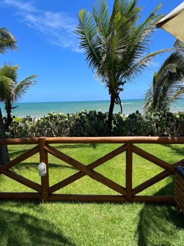 a wooden fence with palm trees and the ocean at Seu cantinho no paraíso de Guarajuba - Bahia in Guarajuba
