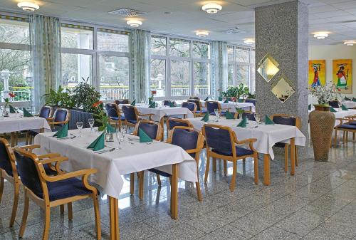 ein Restaurant mit weißen Tischen, Stühlen und Fenstern in der Unterkunft Hotel & Residenz Am Kurpark in Schlangenbad