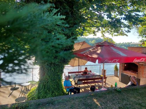 a group of people sitting at a picnic table under a red umbrella at Vikendica Drinski mir in Loznica