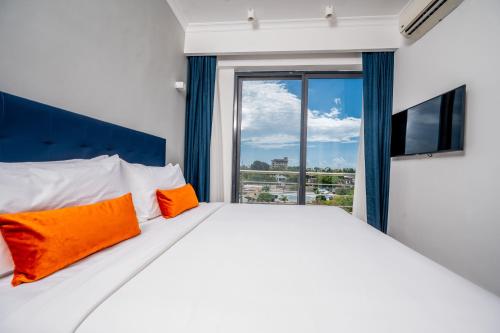 a white bed with orange pillows in a room with a window at Urban by CityBlue Hotel, Dar es Salaam in Dar es Salaam