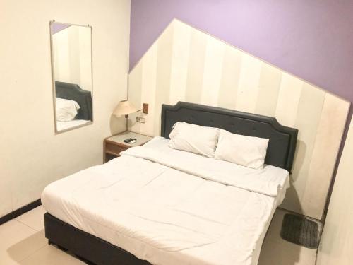 Dormitorio con cama con cabecero de rayas y espejo en Gangnam Style Residence Mitra RedDoorz near MERR Surabaya, en Surabaya