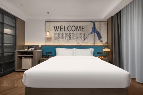 a bedroom with a large white bed and a welcome sign at Mehood Hotel Huangshan High-Speed North Station in Huangshan