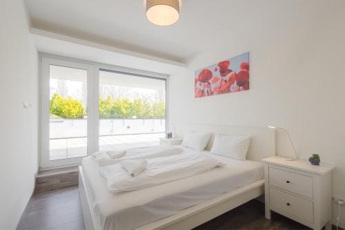 a white bedroom with a large bed and a window at Marina Apartman Balatonszemes by BLTN in Balatonszemes