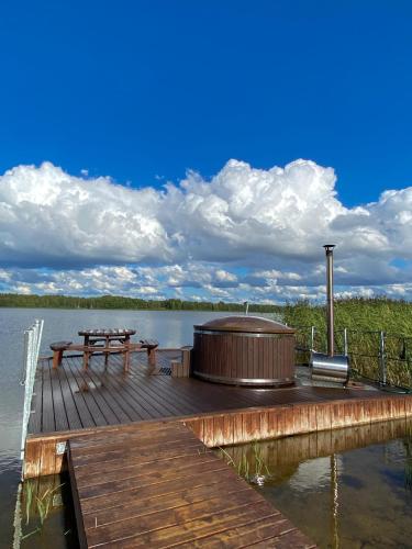 a wooden dock with a hot tub and picnic tables on a lake at Jaundzirnieki in Valdemārpils