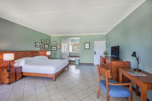 a bedroom with a bed and a desk and a television at Outrigger Mauritius Beach Resort in Bel Ombre