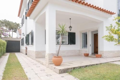 a white house with a potted plant in a yard at Nini Beach House in Aroeira