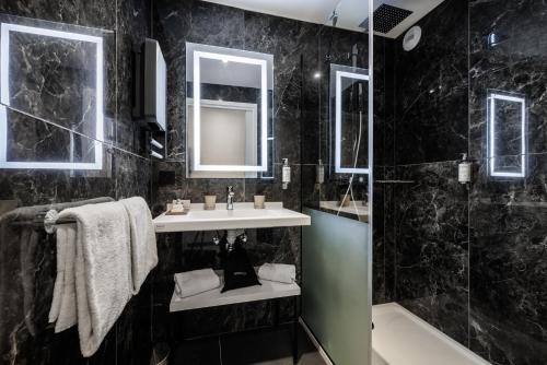 a black tiled bathroom with a sink and a shower at Hôtel Restaurant La Vallée Noble in Soultzmatt