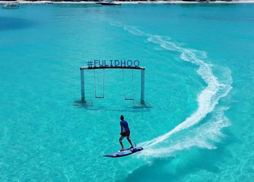a man riding a paddle board in the water at Madi Grand Maldives in Fulidhoo