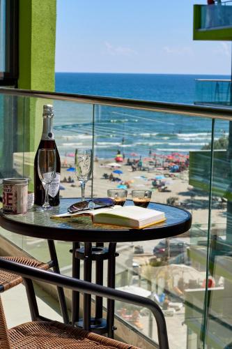 een tafel met glazen en een boek op een balkon met uitzicht op het strand bij Dezactivat D26 in Mamaia Nord – Năvodari