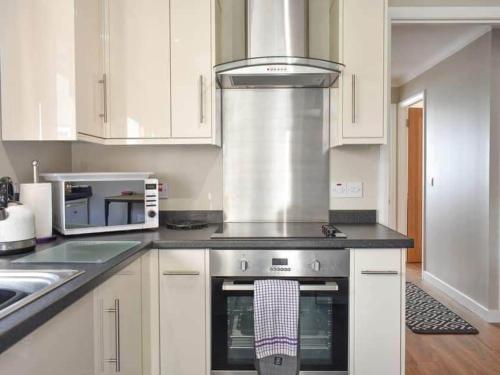 a kitchen with white cabinets and a stove top oven at Cathwill - Cosy 4 Star Cottage - Cairngorm National Park in Newtonmore