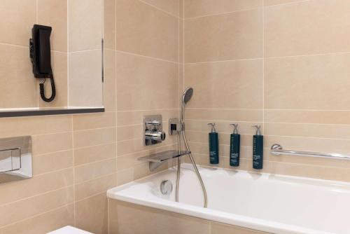 a bathroom with a bath tub with a phone on the wall at Hilton at St George's Park in Burton upon Trent