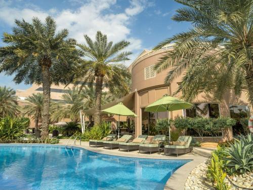 ein Resortpool mit Stühlen und Palmen in der Unterkunft Mövenpick Hotel Bahrain in Manama