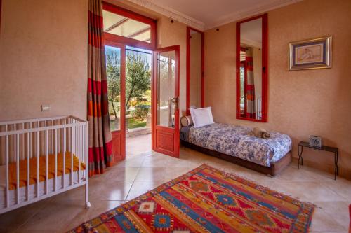 a bedroom with a crib and a bed and a mirror at La Ferme de LallaDom in Tameslouht