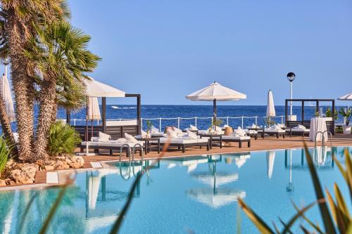 a swimming pool with chairs and the ocean in the background at AluaSoul Menorca - Adults Only in S'Algar
