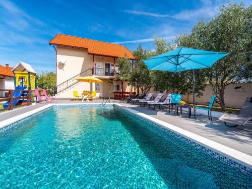 a swimming pool with chairs and a blue umbrella at Holiday Home Villa Vesna Lux in Zadar