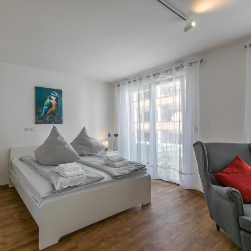 a white bedroom with a bed and a chair at IMMOCITY Apartments Ost in Darmstadt
