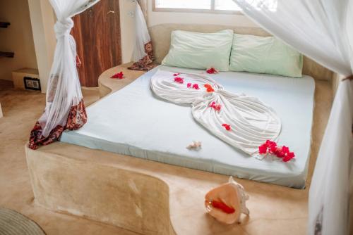 a bed with white sheets and red flowers on it at Marvelous Zanzibar in Jambiani