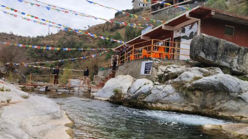 un edificio junto a un río con banderas de oración en Rivulet Resort & Camping en Mussoorie