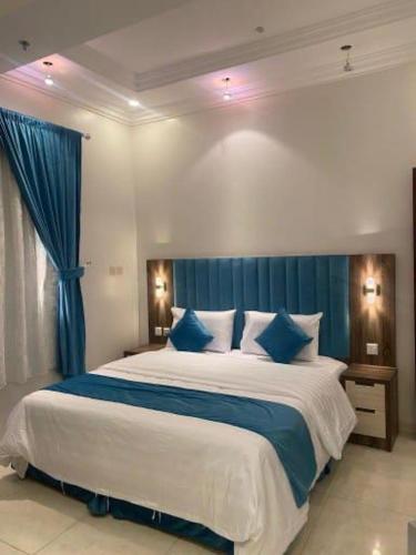 a bedroom with a large bed with blue curtains at فنون راحتي للشقق المخدومة in Shariyah