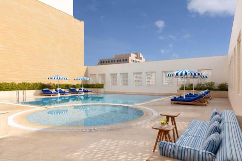 a swimming pool with blue chairs and umbrellas at Al Najada Doha Hotel by Tivoli in Doha