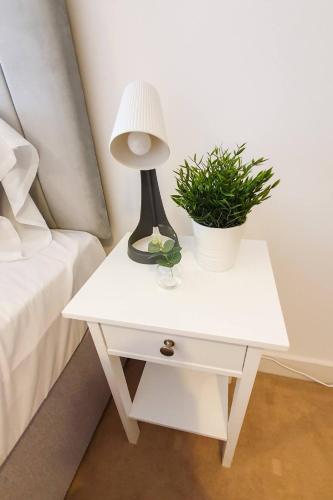 a white nightstand with a lamp and a plant on it at Lovely Flat In Kiln Close With Free Parking in Gloucester
