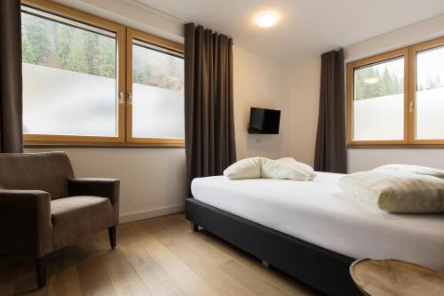 a bedroom with a bed and a chair and windows at Aparthotel Herzblick GmbH in See