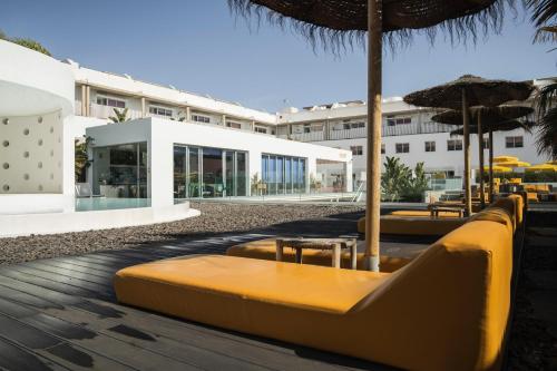 a row of tables and chairs with umbrellas and a building at Buendía Corralejo Nohotel in Corralejo