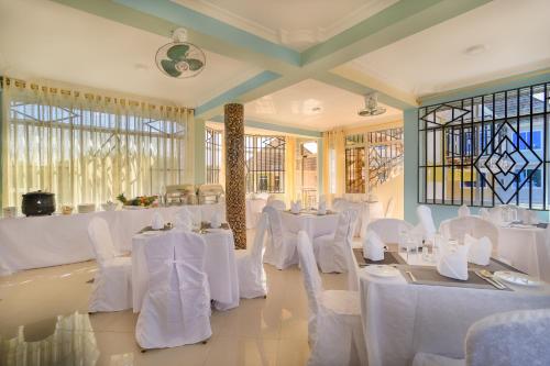 um quarto com mesas e cadeiras brancas e janelas em New Mazubu Grand Hotel Mererani em Mbuguni