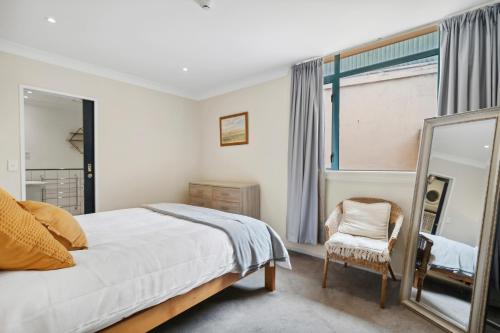 - une chambre avec un lit, un miroir et une chaise dans l'établissement The Urban Charmer - Wellington Holiday Apartment, à Wellington