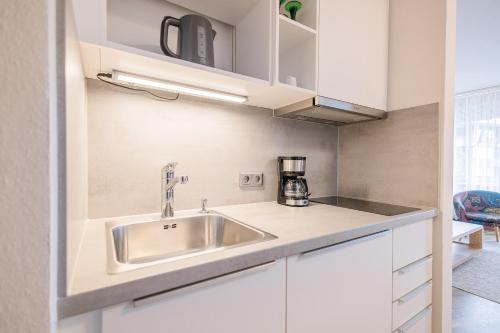 uma cozinha com um lavatório de aço inoxidável e armários brancos em Ferienwohnpark Immenstaad am Bodensee Ein-Zimmer-Apartment 53 19 em Immenstaad am Bodensee