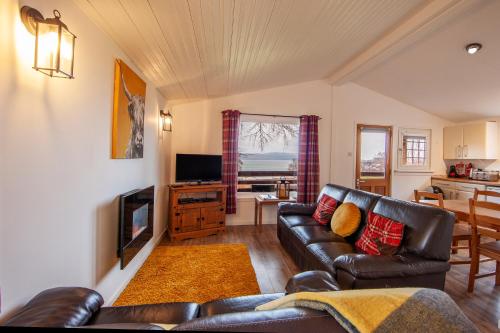 a living room with a leather couch and a television at Appin Holiday Homes -Caravans, Lodges, Shepherds Hut and Train Carriage stays in Appin