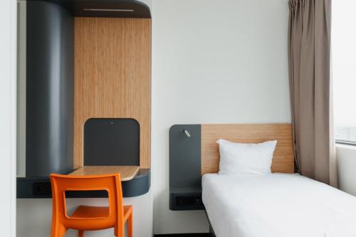 a small bedroom with a bed and a orange chair at easyHotel Amsterdam Zaandam in Zaandam