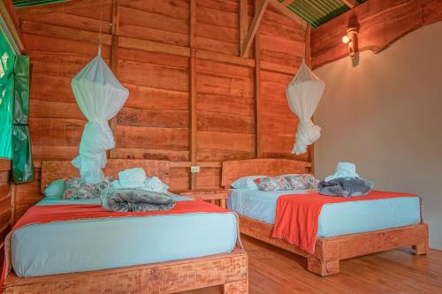 two beds in a room with wooden walls at La Tigra Rainforest Lodge in Fortuna