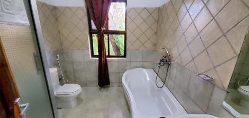 La salle de bains est pourvue d'une baignoire, de toilettes et d'une fenêtre. dans l'établissement NGORONGORO CORRIDOR LODGE Karatu, à Karatu