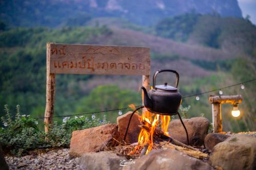 a tea kettle over a fire with a sign at Camping phutajoy Khaosok แคมป์ปิ้งภูตาจ้อยเขาศก in Ban Thung Lang Tham