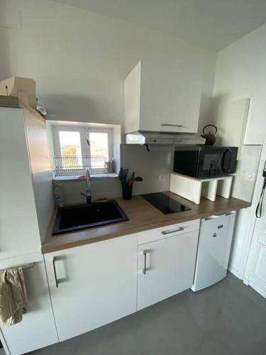 eine weiße Küche mit einer Spüle und einer Mikrowelle in der Unterkunft Appartement vu sur mer Bidart in Bidart