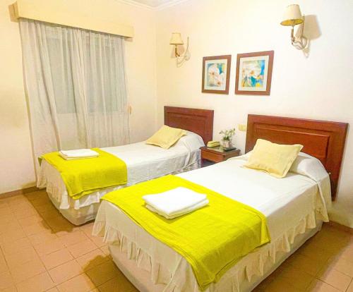 two beds in a hotel room with yellow sheets at Nuevo Hotel Bristol in Santiago del Estero