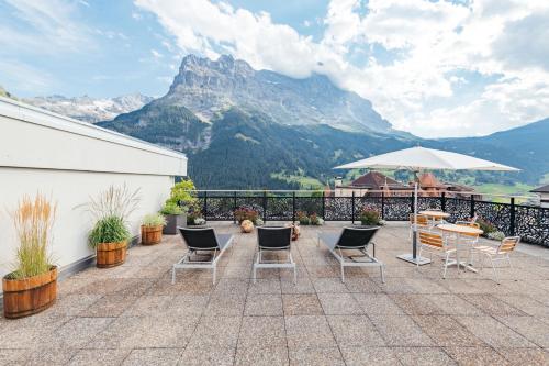 eine Terrasse mit Stühlen, einem Tisch und einem Sonnenschirm in der Unterkunft Hotel Kreuz&Post**** Grindelwald in Grindelwald