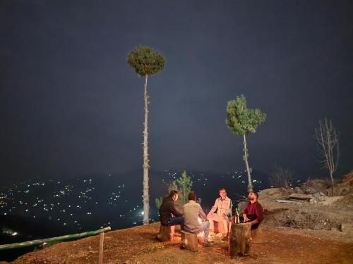 a group of people sitting around a fire on a hill at Gadegal Homestay Narkanda - Rooms & Pahadi Café in Shimla