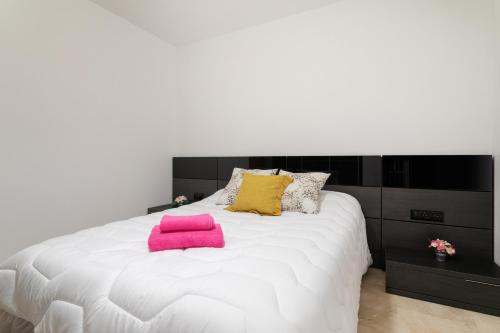 a white bed with pink and yellow pillows on it at 10 minutos de la playa in Asprillas