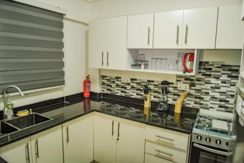 een keuken met witte kasten en zwarte aanrechtbladen bij Impeccable 1-Bed Airbnb in Borteyman in Kwedonu