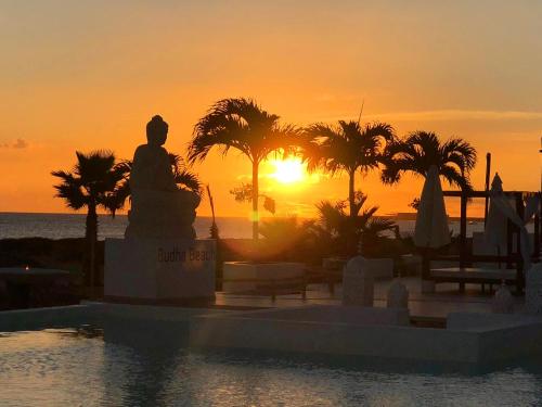 a sunset over the ocean with a statue and palm trees at Hotel LIVVO Budha Beach in Santa Maria