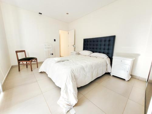a white bedroom with a large bed and a chair at Espacio Chacabuco in Comodoro Rivadavia