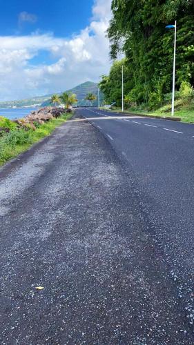 an empty road next to the ocean with trees at Maison de charme à Gourbeyre avec vue mer et montagnes in Gourbeyre
