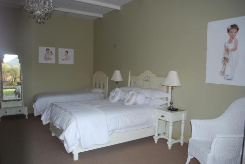 a white bedroom with two beds and a chair at Olive Hill Country Lodge in Bloemfontein